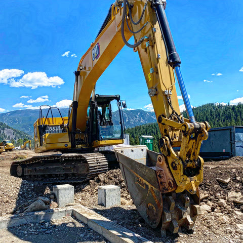 A tracked excavator with a Felco compaction wheel works over rough-graded dirt and pier footings