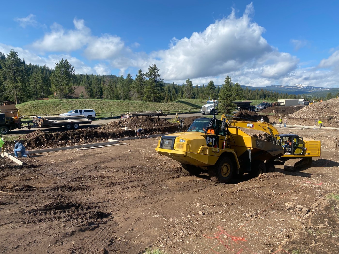 A Cat excavator loads an articulated haul truck on an active cut while crews build forms behind