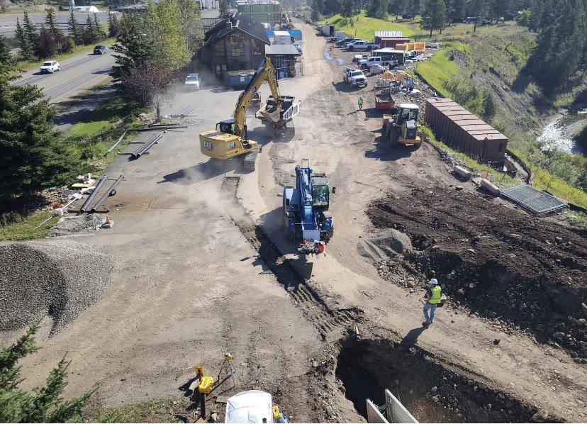 Elevated view of an active utility corridor with excavators, a loader, and a telehandler along a creek