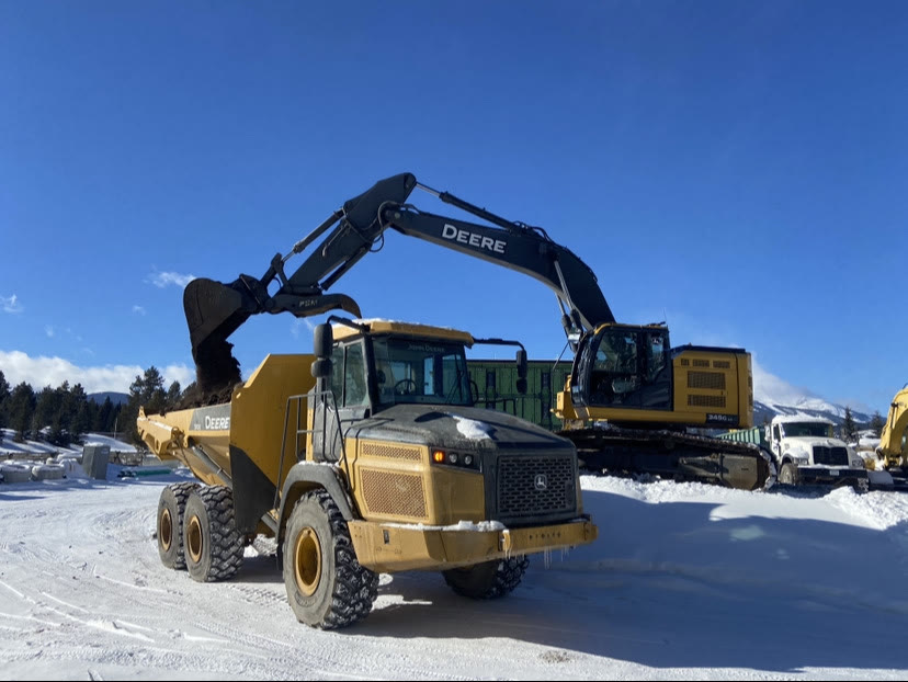 An articulated haul truck loaded by an excavator on a snowy site under blue sky