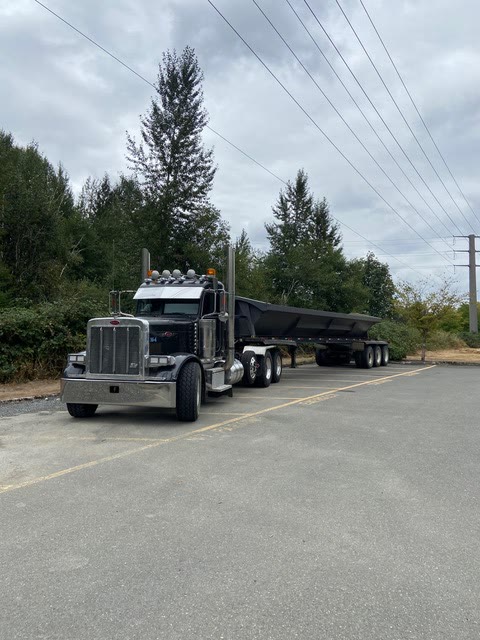 A Peterbilt tractor with a side-dump trailer staged in a paved yard