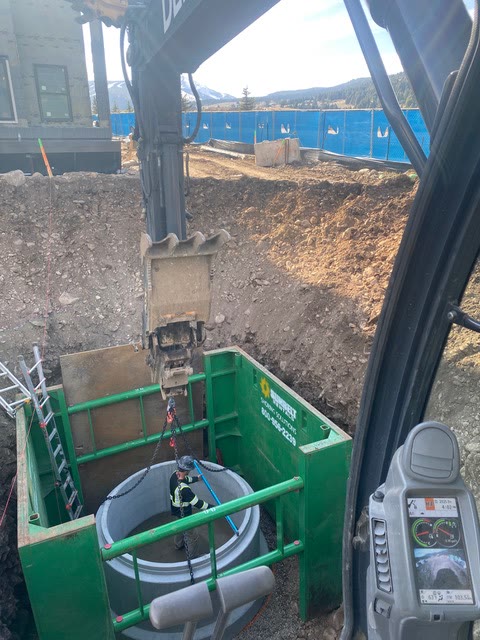 A concrete manhole ring lowered into a shored excavation