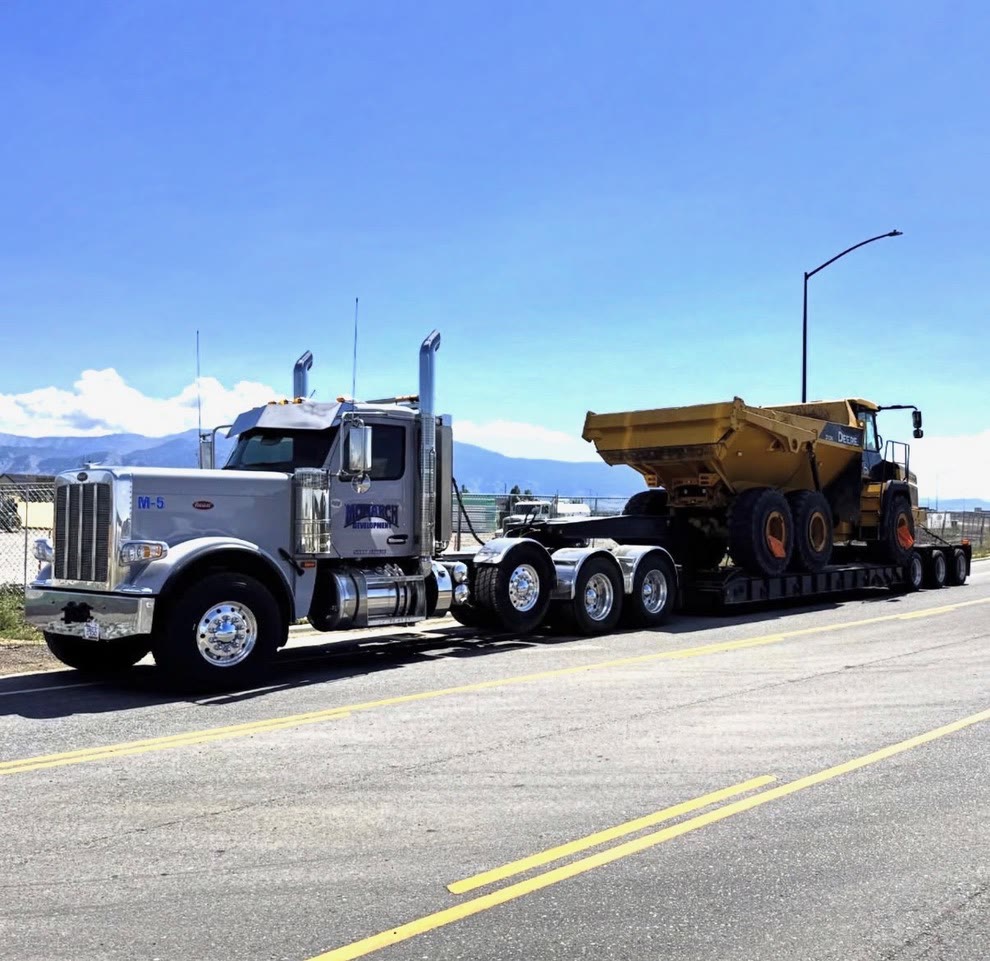 A Monarch Development lowboy hauls an articulated dump truck down a highway